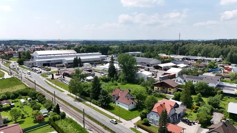 Luftaufnahme einer ländlichen Gegend mit Wohngebäuden, Gewerbeflächen und viel Grün unter blauem Himmel.
