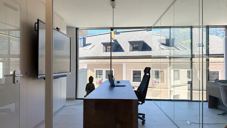 Modernes Büro mit großen Glasfronten, Blick auf die Stadt und die Berge.