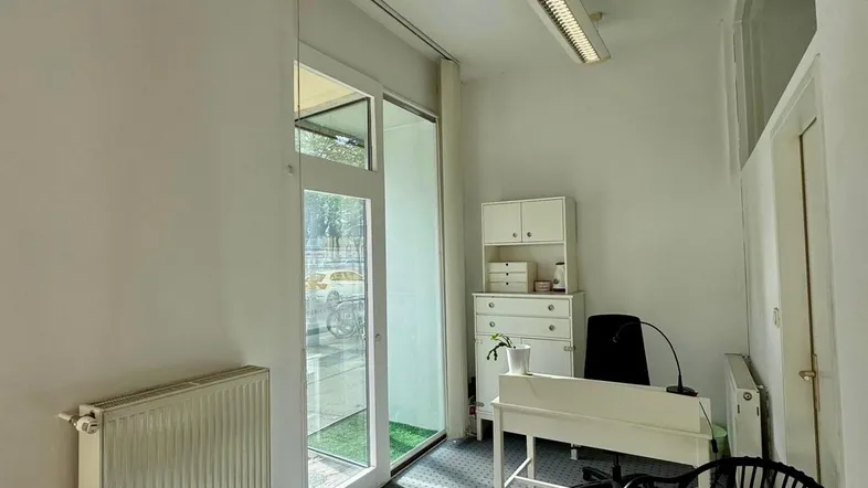 Helles Büro mit Teppichboden, Schreibtisch und Zugang zu einem kleinen begrünten Außenbereich.