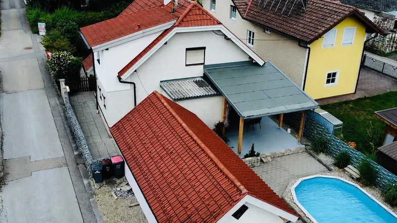Luftaufnahme eines Einfamilienhauses mit rotem Ziegeldach, Garten und einem blauen Swimmingpool.