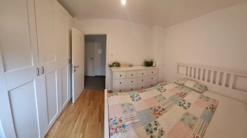 Helles Schlafzimmer mit Holzboden, weißen Einbauschränken und einem gemütlichen Bett.