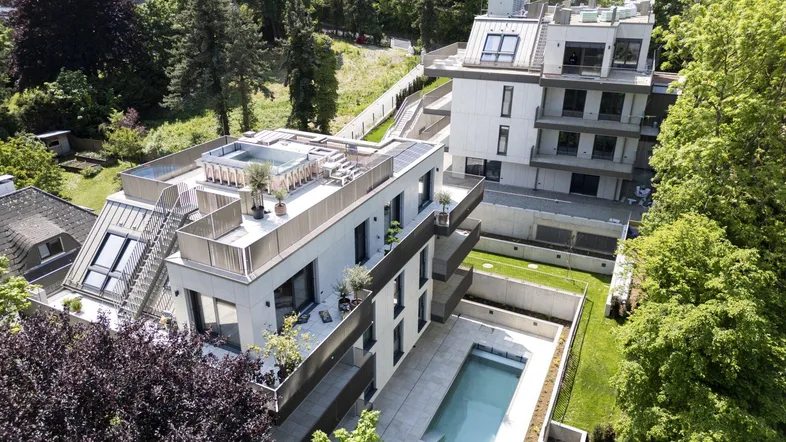 Luftaufnahme moderner Wohngebäude mit Dachterrassen, einem Pool und umgebender grüner Landschaft.