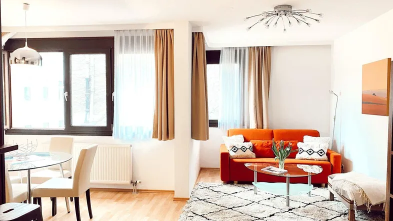 Helles Wohn- und Esszimmer mit Parkettboden, orangefarbenem Sofa und modernem Esstisch.