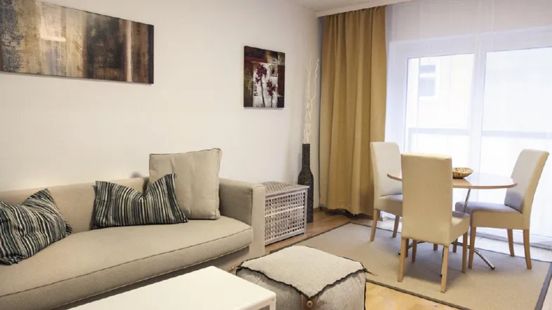 Helles Wohn- und Esszimmer mit beigem Sofa, Holzboden und Zugang zum Balkon.