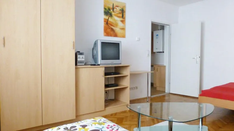 Helles Wohnzimmer mit TV-Möbeln, Kleiderschrank und einem modernen Glastisch.