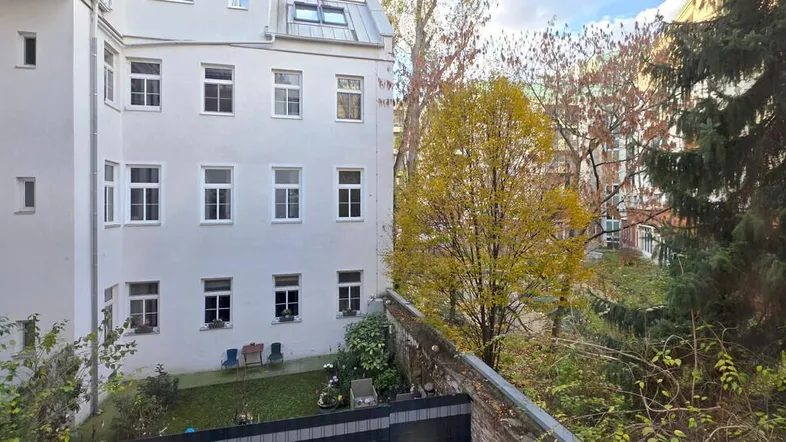 Weißes Mehrfamilienhaus mit vielen Fenstern und Blick auf einen grünen Innenhof mit Herbstbäumen.