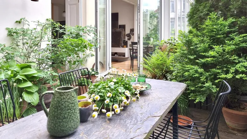 Gemütliche Terrasse mit Steintisch, üppiger Bepflanzung und Zugang zum Wohnbereich.