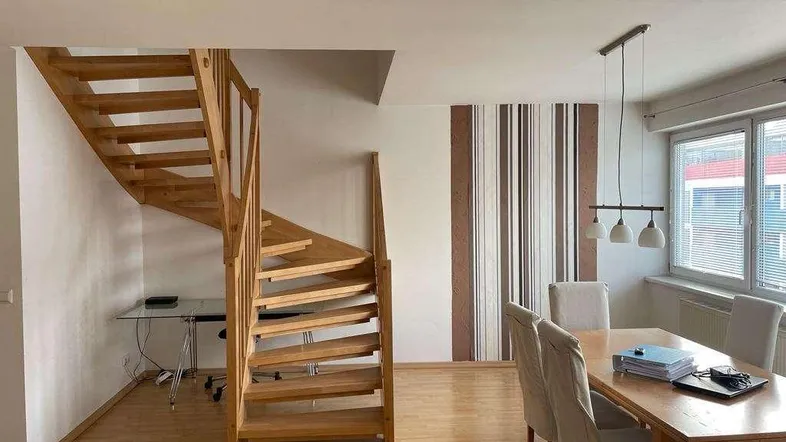 Heller Wohn- und Essbereich mit eleganter Holztreppe und großzügigen Fenstern.