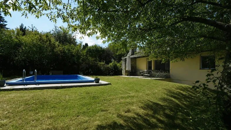 Großer Garten mit Rasenfläche, Swimmingpool und schattenspendenden Bäumen vor dem Haus.