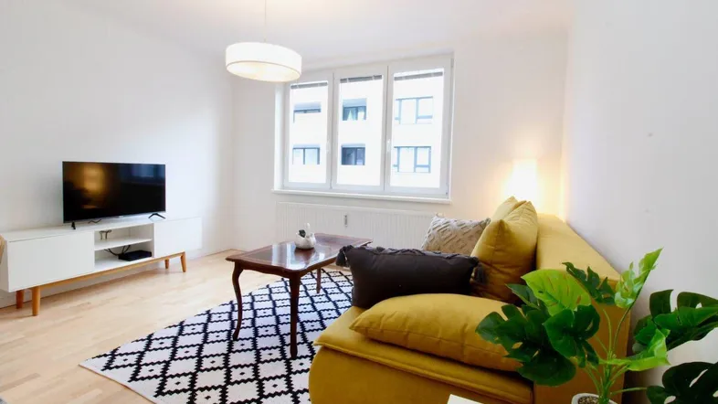 Helles Wohnzimmer mit gelbem Sofa, modernem Teppich und Blick auf die Stadt.