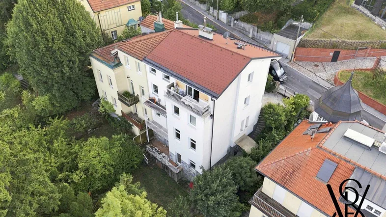 Luftaufnahme eines Mehrfamilienhauses mit rotem Ziegeldach und umgebender grüner Vegetation.