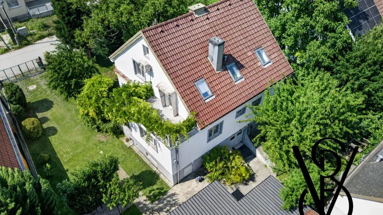 Luftaufnahme eines Einfamilienhauses mit rotem Ziegeldach, umgeben von viel Grün und Bäumen.
