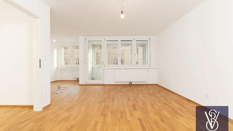 Helles, leeres Wohnzimmer mit Parkettboden und großen Fenstern, bereit zur individuellen Gestaltung.