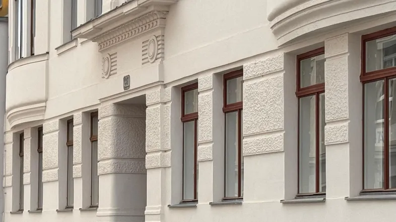 Historische Fassade eines Mehrfamilienhauses mit eleganten Stuckdetails und braunen Fenstern.