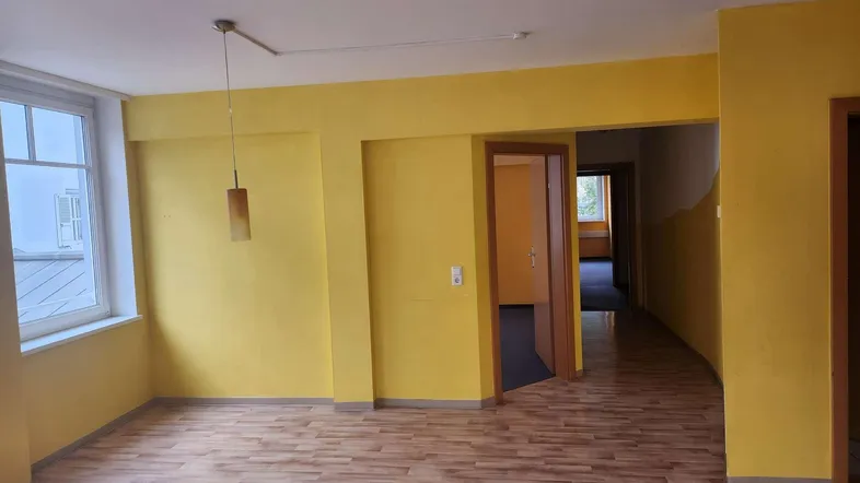 Geräumiger, leerer Raum mit gelben Wänden und Laminatboden, bereit zur individuellen Gestaltung.
