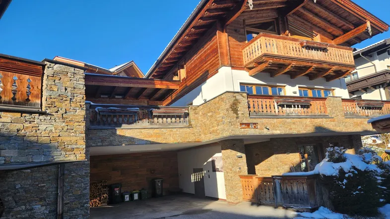 Traditionelles Chalet mit Holzfassade, Steinmauern und Balkonen im winterlichen Ambiente.