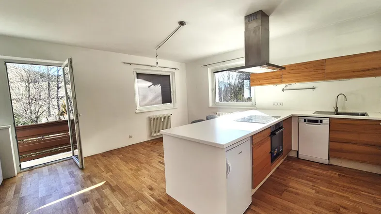 Moderne offene Küche mit Kochinsel, Holzelementen und Zugang zum Balkon.