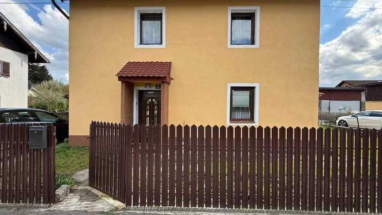 Gelbes Einfamilienhaus mit braunem Holzzaun und Vorgarten unter blauem Himmel.