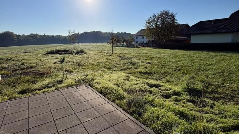 Sonnige Landschaft mit weitem Blick über grüne Felder und eine gepflasterte Fläche im Vordergrund.