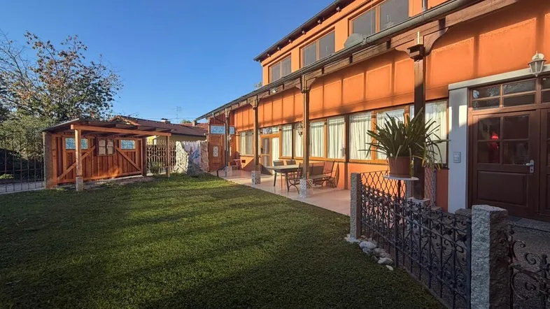 Geräumiger Gartenbereich mit Rasenfläche, überdachter Terrasse und einem Holzschuppen unter blauem Himmel.