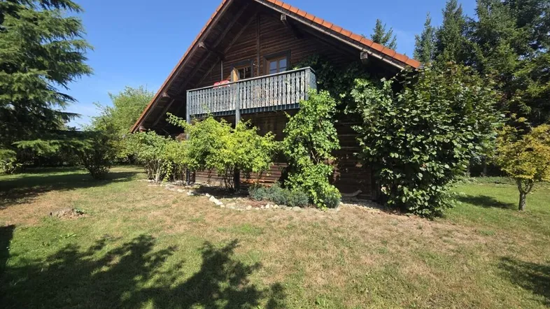 Charmantes Holzhaus mit Satteldach und einem kleinen Balkon, umgeben von viel Grün und Bäumen.