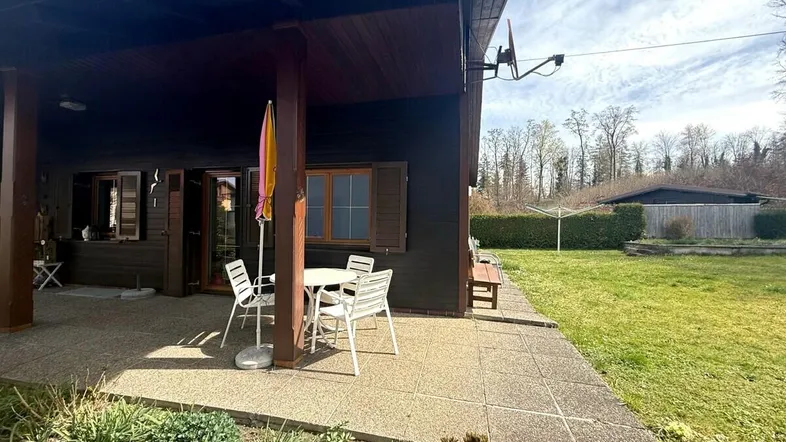 Überdachte Terrasse mit Gartenmöbeln und Blick ins Grüne, umgeben von Rasenfläche.