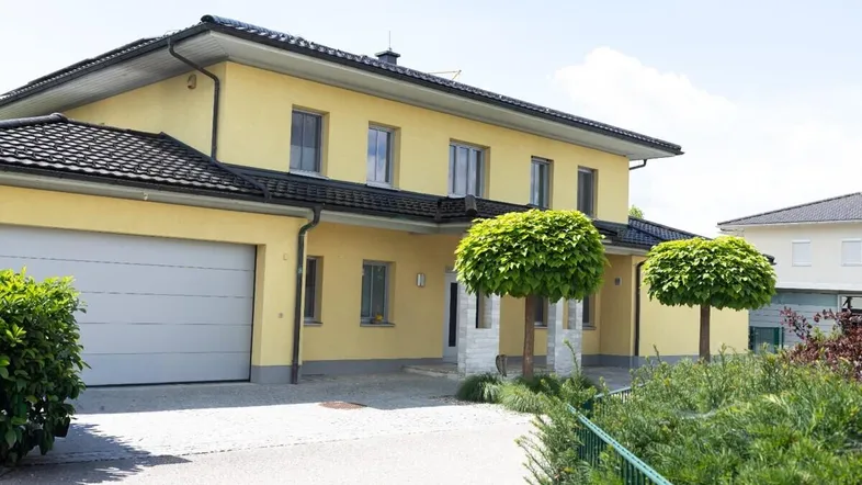 Gelbes Einfamilienhaus mit integrierter Garage und gepflegtem Vorgarten unter blauem Himmel.