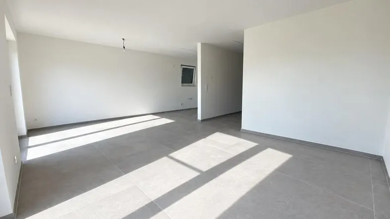 Heller, leerer Wohnbereich mit modernen grauen Fliesen und viel natürlichem Licht.