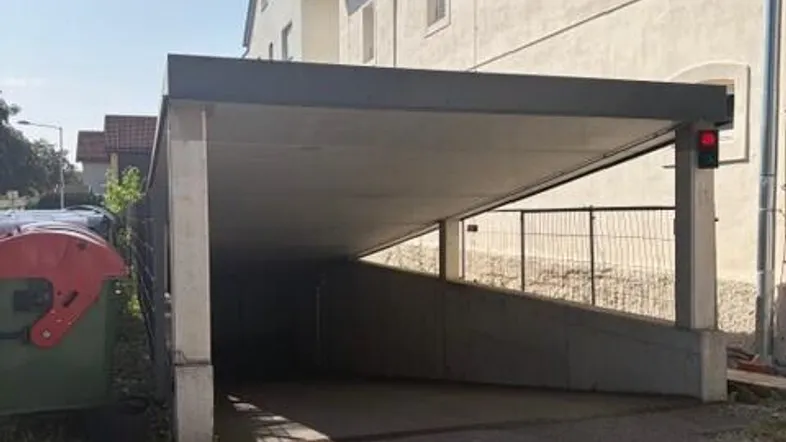 Einfahrt zur Tiefgarage mit überdachtem Bereich und angrenzendem modernen Gebäude.