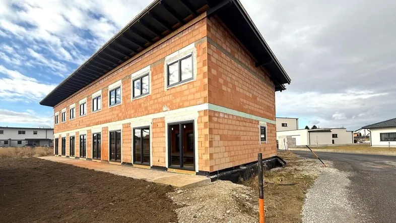 Rohbau eines modernen Gebäudes mit Ziegelwänden und großen Fensteröffnungen.