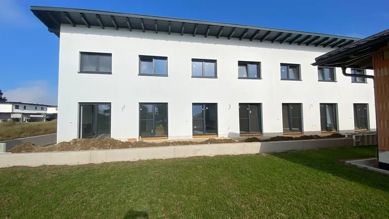 Neubau mit weißer Fassade, vielen Fenstern und Zugang zum Gartenbereich.
