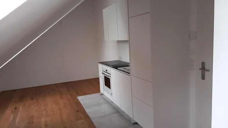 Moderne Küchenzeile in einem hellen Dachgeschossraum mit Holzboden und Schrägdecke.