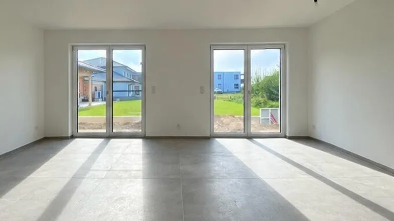 Heller, leerer Raum mit großen Glastüren und Blick ins Grüne, ideal für Wohn- oder Essbereich.