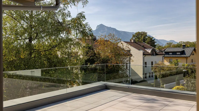 Geräumige Dachterrasse mit Glasgeländer und weitem Blick auf die umliegenden Berge und Bäume.