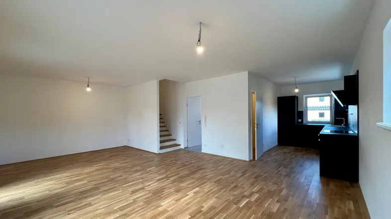 Heller offener Wohnbereich mit Parkettboden und Blick auf die moderne Küche sowie die Treppe.
