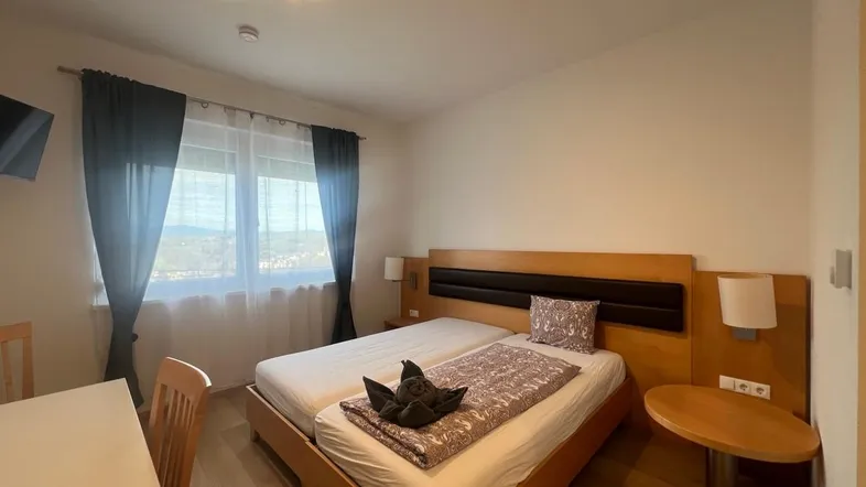 Helles Schlafzimmer mit zwei Einzelbetten, Holzmöbeln, Parkettboden und einem Fenster mit Blick ins Grüne.