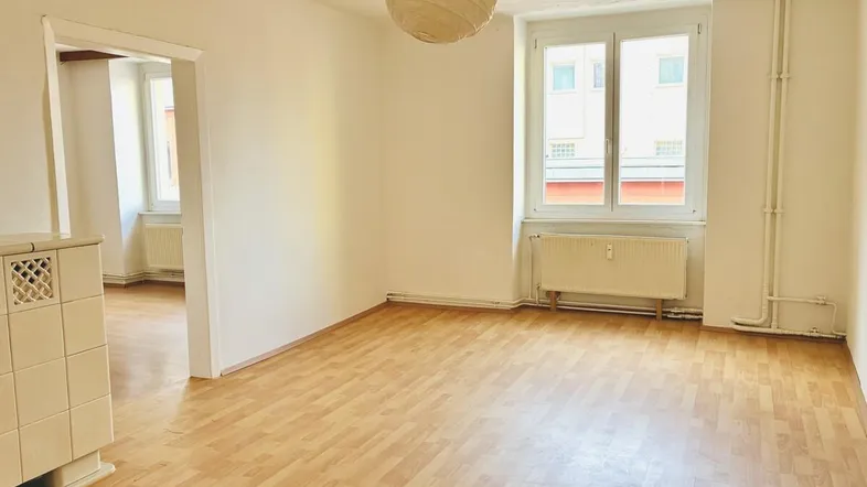 Helles Wohnzimmer mit Parkettboden, weiß gestrichenen Wänden und einem traditionellen Kachelofen.