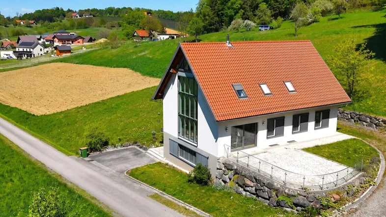 Modernes Einfamilienhaus mit rotem Ziegeldach und großer Terrasse in ländlicher Umgebung.