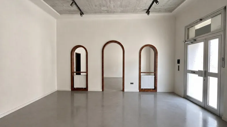 Helles, leeres Zimmer mit Betondecke, modernen Lichtschienen und bogenförmigen Durchgängen.