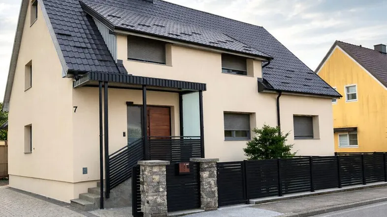Modernes Einfamilienhaus mit beiger Fassade, dunklem Dach und gepflegtem Eingangsbereich.