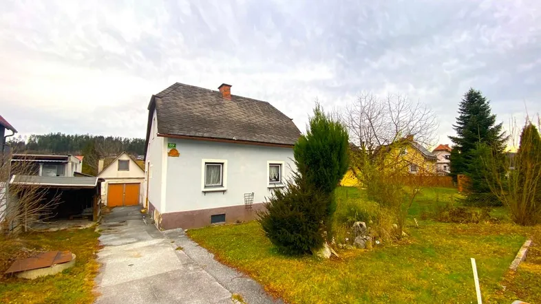 Einfamilienhaus mit heller Fassade, grauem Dach und Vorgarten unter bewölktem Himmel.