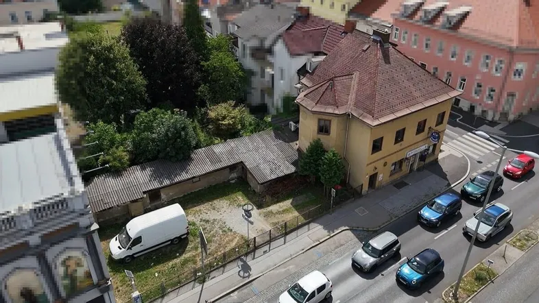 Luftaufnahme eines Gebäudes an einer Straße mit parkenden Autos und umliegender Bebauung.