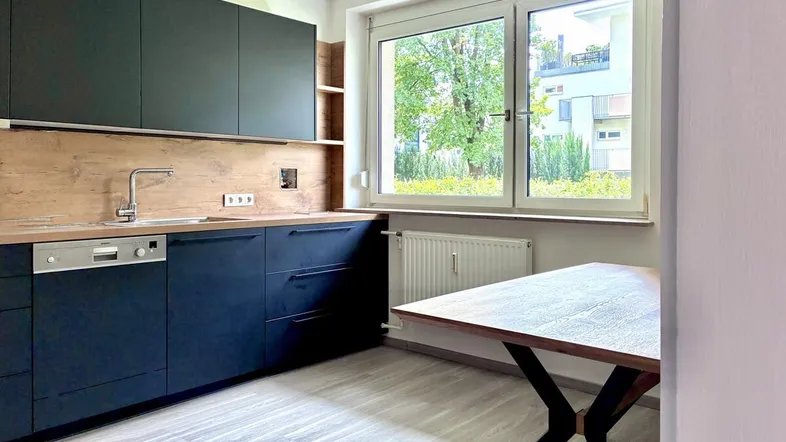Moderne Küche mit dunklen Schränken, Holzakzenten und einem Esstisch am Fenster mit Blick ins Grüne.