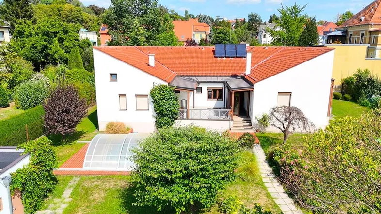 Luftaufnahme des Hauses mit großem Garten, überdachtem Pool und Photovoltaikanlage auf dem Dach.