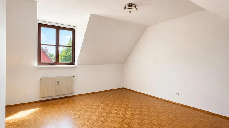 Helles Zimmer im Dachgeschoss mit Parkettboden und schrägen Wänden, ideal als Schlafzimmer.