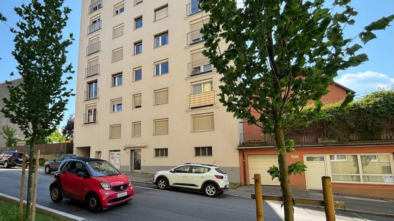 Modernes Mehrfamilienhaus mit mehreren Etagen und Balkonen an einer sonnigen Straße.