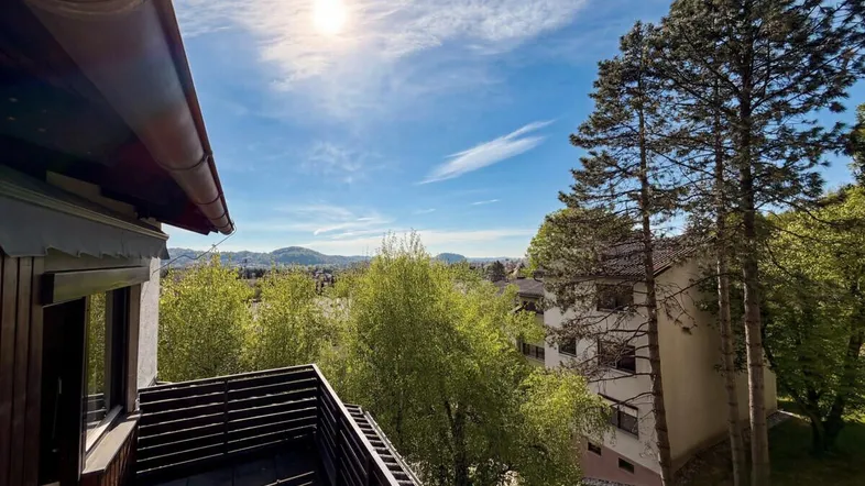 Sonniger Balkon mit Holzboden und weitem Blick über die grüne Landschaft und die Stadt.