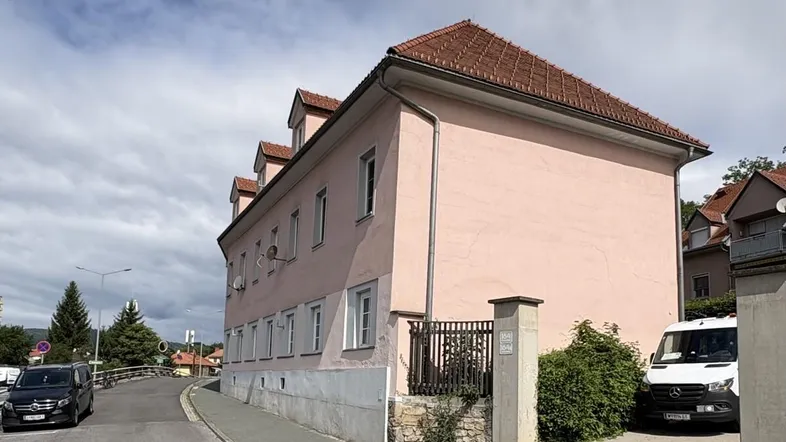 Gebäudeansicht eines rosa gestrichenen Hauses mit Ziegeldach und gepflegter Umgebung.