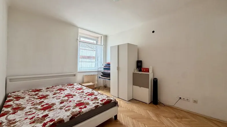 Helles Schlafzimmer mit Fischgrätparkett, einem Bett und einem weißen Kleiderschrank.