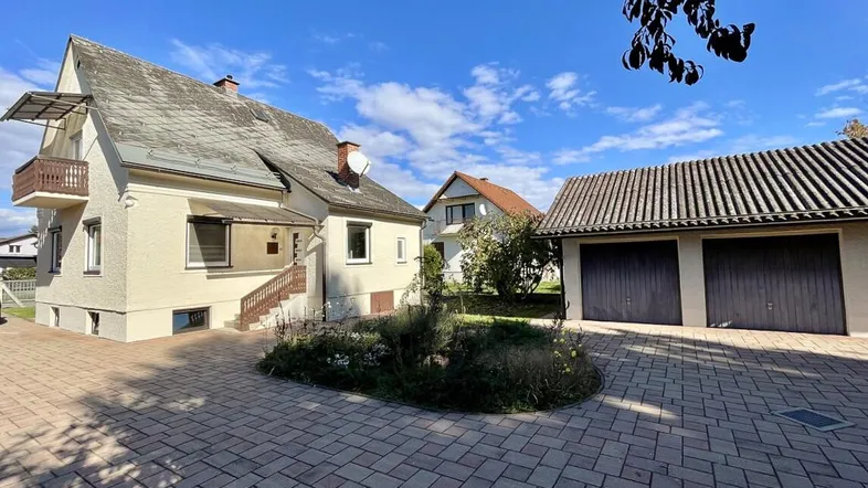 Einfamilienhaus mit gepflasterter Auffahrt, Doppelgarage und Balkon unter blauem Himmel.